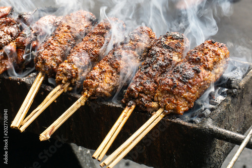 Sate Buntel (Culinary specialty from Solo, Central Java, Indonesia), featuring minced goat meat wrap in fat and grilled over charcoal with billowing smoke. Selective focus