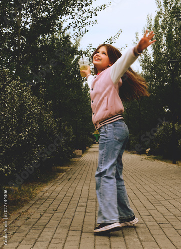 Fotografie Cute smiling girl having fun in the city park, drinking lemonade , street food,  Retro style, nostalgic, dreamy atmosphere, Blurred mootion draws attention to the naturalness of the moment