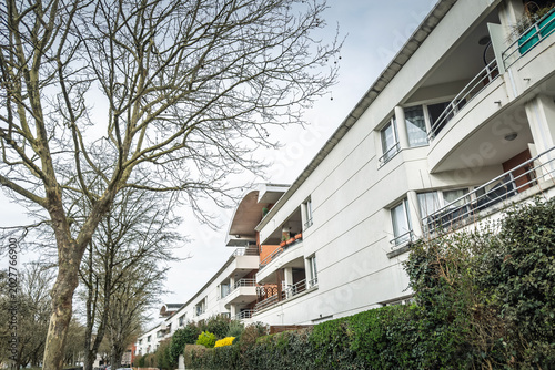 Obraz na płótnie Residential apartment building in a Paris suburb in Ile de France, with balconies, hedges, trees and a quiet pedestrian path beside modern suburban housing and french banlieue
