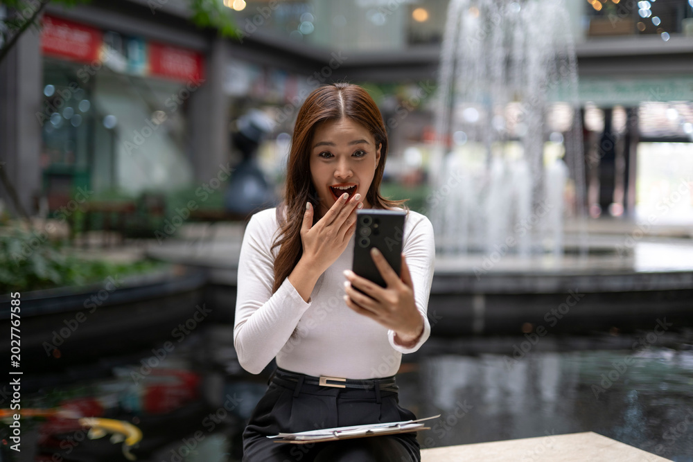 Fototapeta premium Surprised woman reacting to mobile phone content in shopping mall