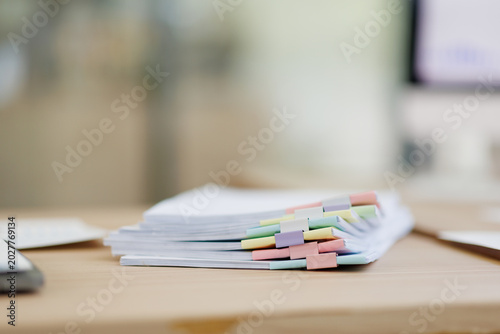 Φωτογραφία Stacked office documents with colorful file tabs and binder clips on a light woo
