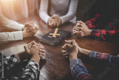 Fotografia Group of Christian  holding hands praying worship together to believe and Bible on a wooden table for devotional for prayer meeting concept, teamwork