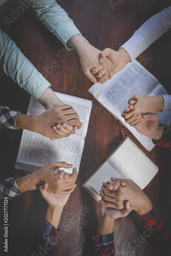 Christian group of people holding hands praying worships together to believe and Bible on a wooden table for devotional for prayer meeting concept. Christian worship and pray.  teamwork.