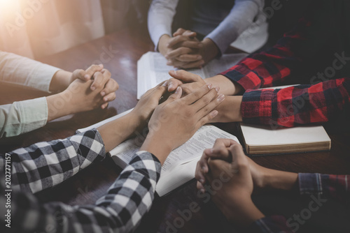 Fotografia Christian group of people holding hands praying worships together to believe and Bible on a wooden table for devotional for prayer meeting concept