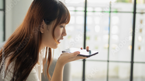 Foto Asian woman sitting using smartphone talking with friend by speakerphone