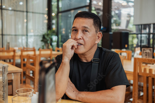 Foto Middle-aged Filipino man looks impatient and bites nails while waiting alone at a Southeast Asian restaurant or bar