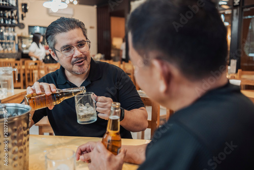 Φωτογραφία A middle aged man enjoys a light conversation with his friend while pouring beer