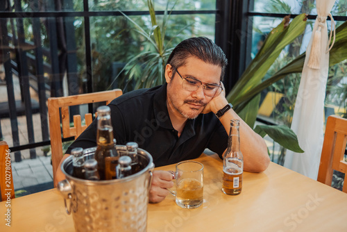 Fényképezés A man drinking beer at the bar while thinking deeply alone, resting his head on his hand and staring at his glass, appearing worried and contemplative, reflecting on personal problems
