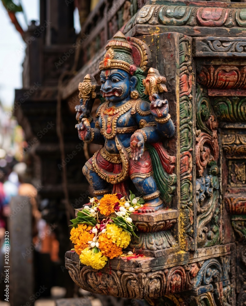 Fototapeta premium Ornate carved wooden figure on a temple chariot bracket with fresh flower offerings for cultural heritage tourism, traditional festival promotion and religious art editorial