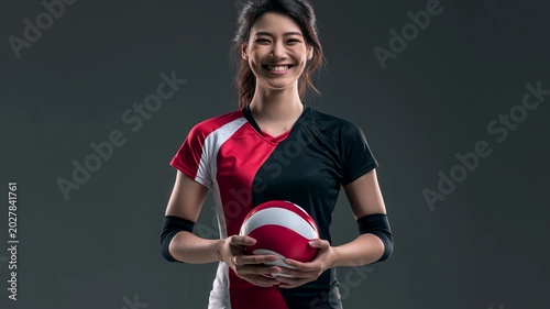 Asian female volleyball athlete holding ball wearing red and black uniform with elbow pad confident sport player focused full body portrait dark