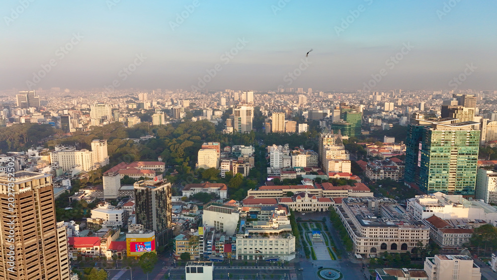Fototapeta premium Ho Chi Minh City, Vietnam – 4K aerial sunrise drone view of downtown skyline with modern skyscrapers, dense urban housing, busy streets and morning traffic along the Saigon River in Southeast Asia