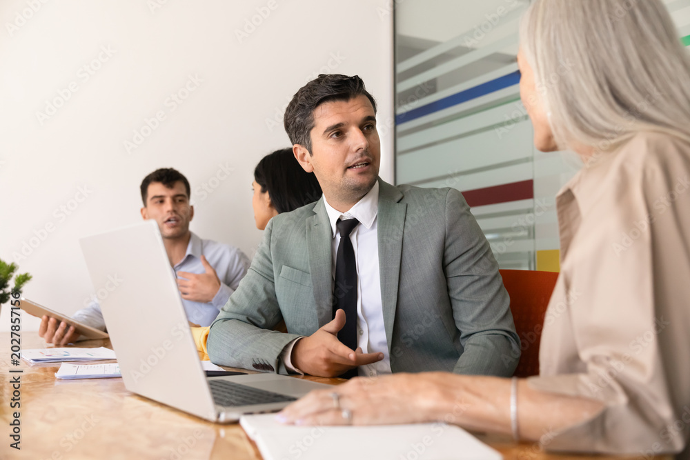 Obraz premium Businessman speaking with woman colleague at conference table, discussing ideas, explaining strategy, consulting corporate client during professional office meeting. Communication, teamwork, business