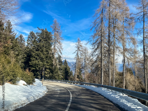 Snowy winter road winding through a forest in the mountains under a cold blue sky