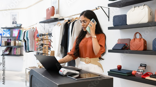 Obraz na plátně Indian woman stands at checkout counter of modern boutique, having business conv