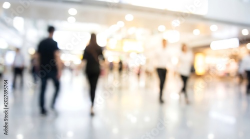 Blurred crowd of people walking through a bright modern shopping mall or convention center lobby with soft bokeh lighting for commercial and business background concepts
