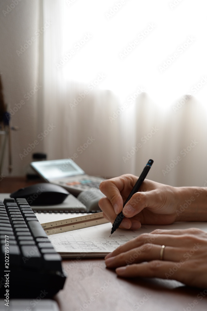 Fototapeta premium Architect writing design notes at desk with keyboard and calculator キーボードと電卓のあるデスクで設計メモを書く建築士の手元