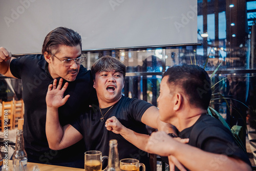 Foto Young man intervenes between two arguing friends at a bar, preventing a fight while drinks sit on the table during tense moment