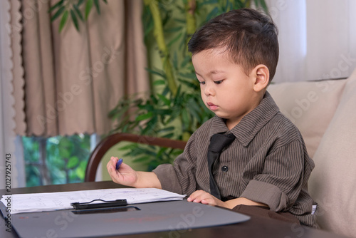 A 2-year-old little boy sitting at the table looking down at the clipboard