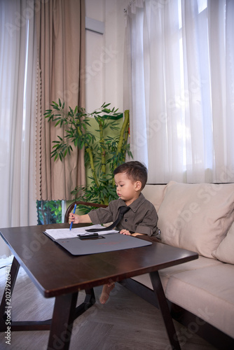A 2-year-old little boy sitting at the table in the background writing on paper