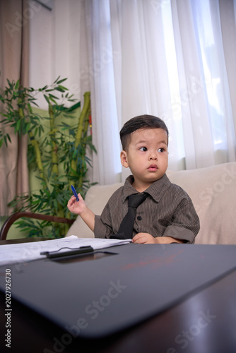 A 2-year-old toddler boy sitting on the sofa holding a blue pen and looking at the camera