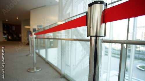 Canvastavla A retractable red belt barrier mounted on a stainless steel stanchion in a moder