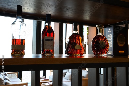 Four bottles of cognac are arranged in a row on a wooden shelf, with some labels visible and one bottle placed next to its box