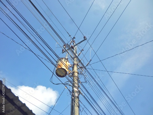 Low angle view of electrical utility pole with transformer and tangled wires against blue sky