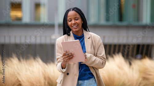 Black woman smiling using tablet in city park