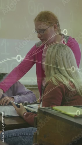 Vertical video: Standing student reaching tablet, guiding peer in class as nodes overlaying device