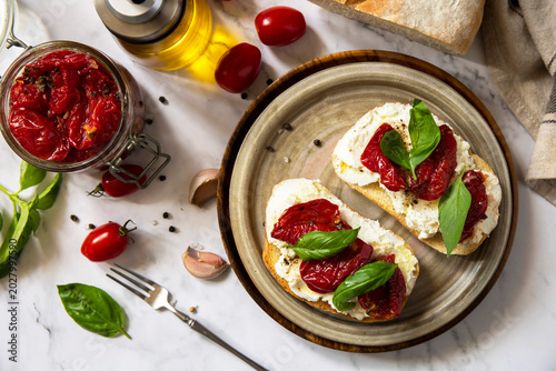 Open sandwiches or bruschetta with cream cheese and sun dried tomatoes on a stone table. Healthy food. Delicious breakfast or wine snack. View from above.