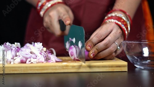 Indian woman hands slicing red onion on wooden board for cooking. Close up of South Asian housewife chopping red onion with sharp knife.