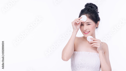 Fotografía Beautiful young Asian woman with flawless skin holding two white cotton pads on her face isolated on white background