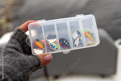 Fotografie Hand holding a clear tackle box filled with fishing lures spinner tail