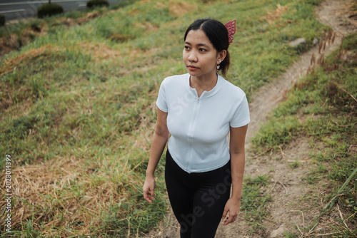 Fotografie Young Southeast Asian woman walking thoughtfully in a grassy trail outdoors