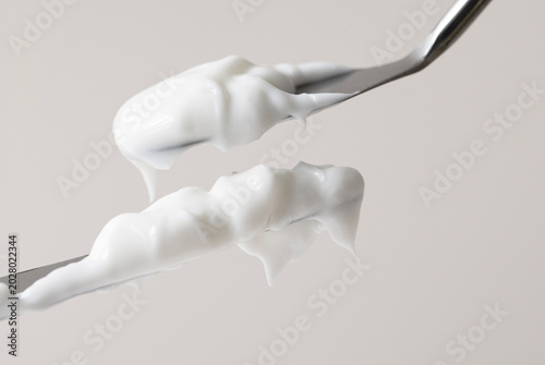 Two spatulas with samples of white moisturizer close-up front view, beige background.