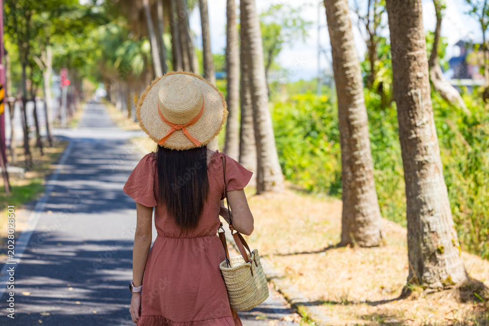 Fototapeta premium Back view of woman with hat walking in sunny park
