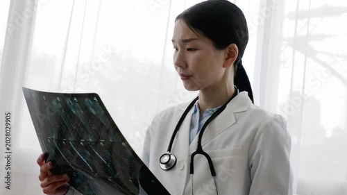 Asian Female Doctor in White Coat Reviewing X-ray Image