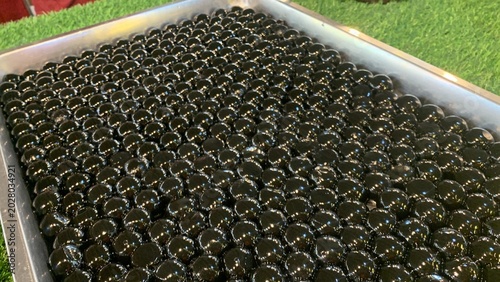 Glossy black tapioca pearls, often referred as giant boba pearls on aluminum tray, infused with flavors like brown sugar or caramel to enhance their taste. commonly used in specialty bubble tea drinks