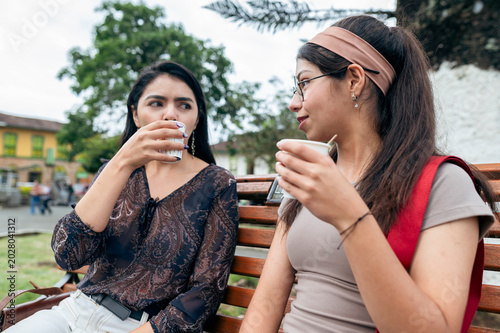 Young women socializing drinking coffee in park
