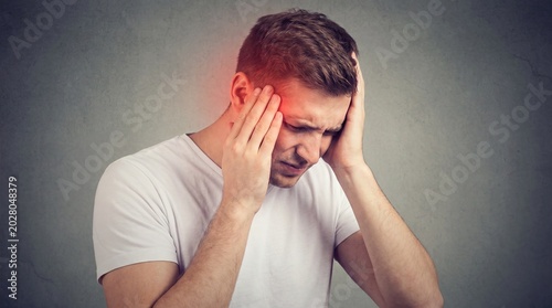 Young man suffering from headache holding head in pain facing gray background