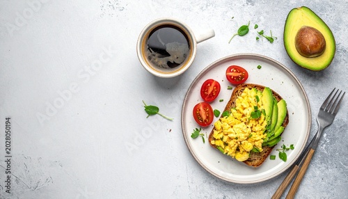 Healthy breakfast with avocado toast, scrambled eggs, cherry tomatoes, and a cup of coffee on a light background, viewed from above.