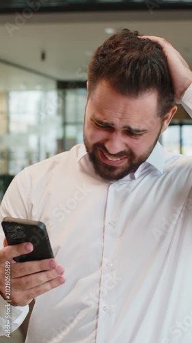 Businessman in formal shirt using smartphone typing browsing, loses becoming surprised sudden lottery results bad news, fortune loss fail office lobby. Upset entrepreneur guy with mobile phone in hall