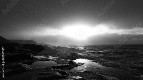 Dramatic Black and White Coastal Landscape with Powerful Waves Crashing Against Rocky Shoreline at Sunset