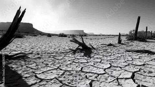 Black and White Wide Angle View of Barbed Wire Fence and Cracked Earth Under a Bright Sky in a Desert Landscape