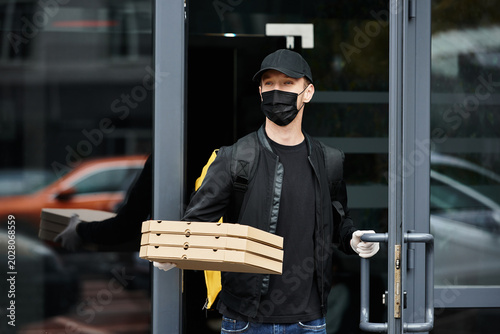 Fotografija Young man delivers fresh pizza boxes while wearing gloves and a mask in a bustli