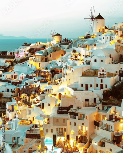 Whitewashed Santorini homes and glowing windmills shine above the Aegean Sea at dusk, creating a magical Mediterranean escape filled with romance, timeless beauty, and peaceful island charm.