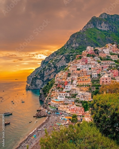 Colorful seaside village glows at sunset beneath towering cliffs, where golden skies and Mediterranean waters create a breathtaking coastal paradise full of romance and beauty.