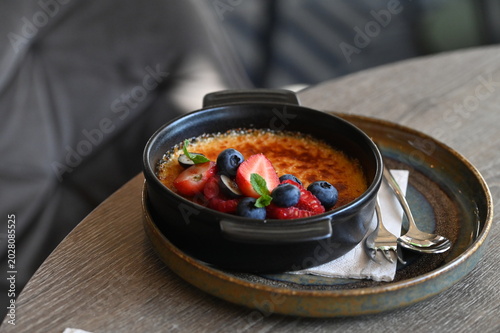 Fotografie French crème brûlée dessert with fresh fruit served in a black bowl