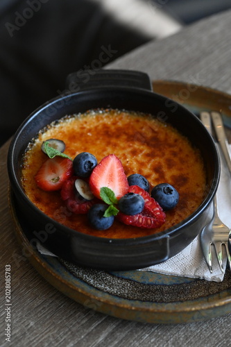 Fotografie French crème brûlée dessert with fresh fruit served in a black bowl