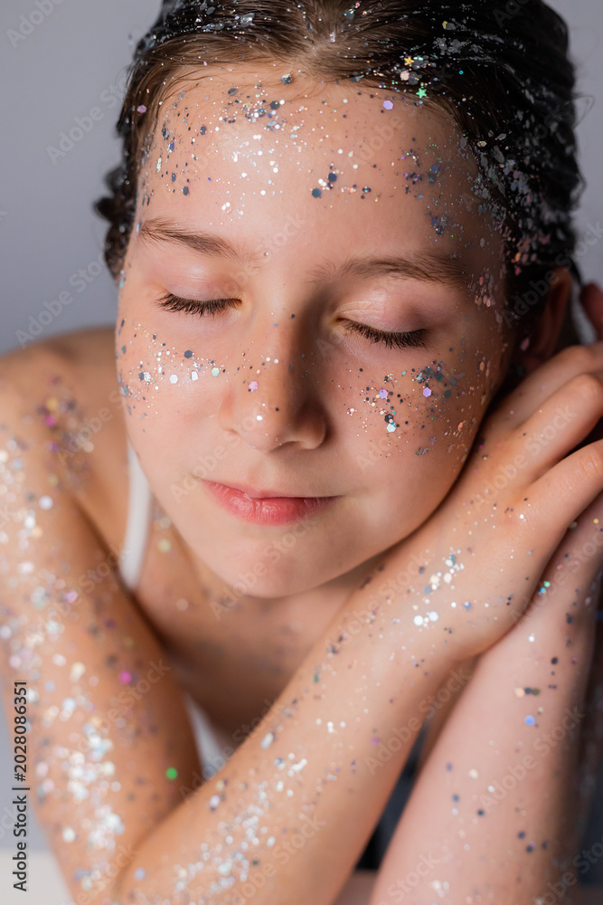 Naklejka premium portrait of a little girl with blue eyes and glitter on her face in a studio on a light background